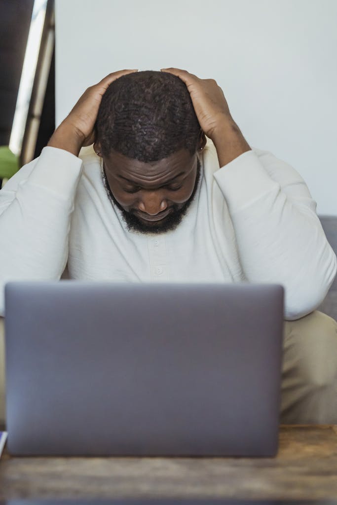 Black man lowering head sitting in front of laptop