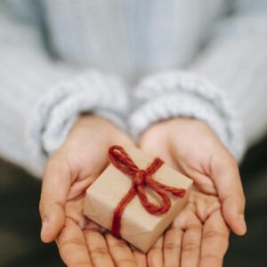 High angle crop unrecognizable female in blue sweater demonstrating small wrapped present box on hands