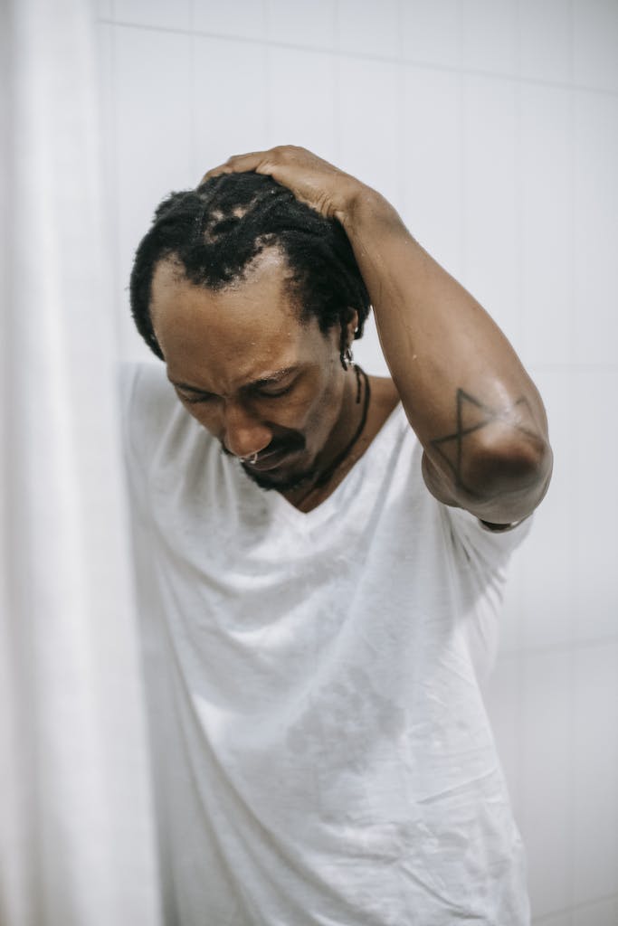 Unhappy black man touching head in shower